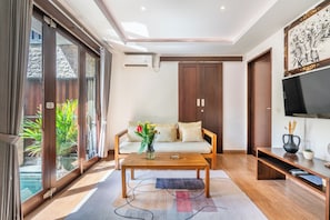 A modern living room with a sofa, coffee table, TV, and a large window. - Chic 2BR Private Pool Villa Seminyak, Enclosed AC Living & Fast Wi-Fi (Badung)