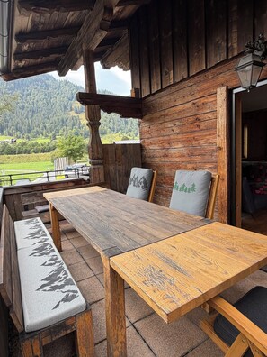 Un espace de restauration extérieur en bois, avec des bancs et une table, offrant une vue sur un paysage montagneux.