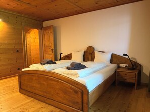 Un lit en bois avec une literie blanche, une table de chevet avec une lampe et une porte en bois.