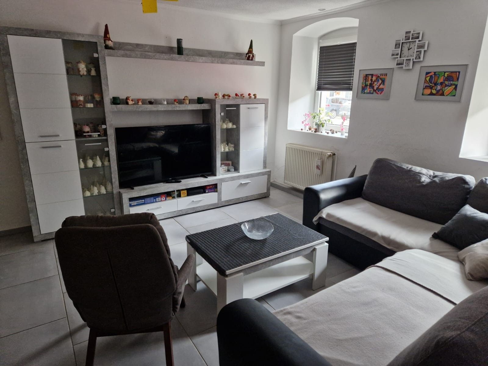 A modern living room with a flat-screen TV, a sofa, a coffee table, and a cabinet with decorative items.