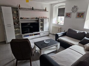 A modern living room with a flat-screen TV, a sofa, a coffee table, and a cabinet with decorative items. - Holiday Apartment 'Lucy' with Shared Terrace, Shared Garden and Wi-Fi (Nattenheim)