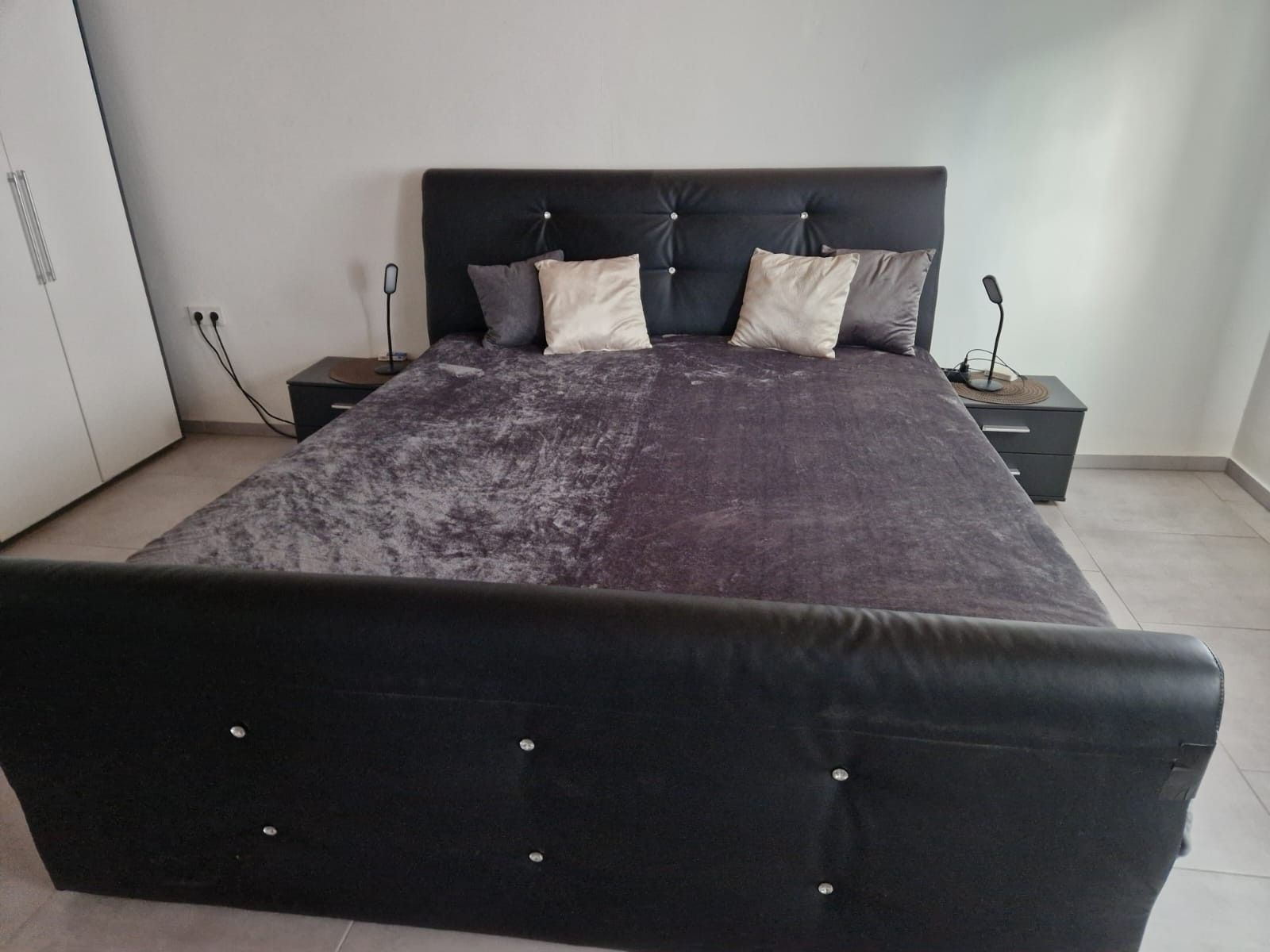A bedroom with a large bed, two bedside tables, and a wardrobe.