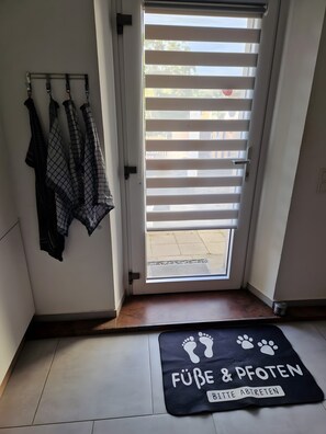 A room with a sliding door, a tiled floor, a doormat with paw prints, and a rack with folded clothes. - Holiday Apartment 'Lucy' with Shared Terrace, Shared Garden and Wi-Fi (Nattenheim)