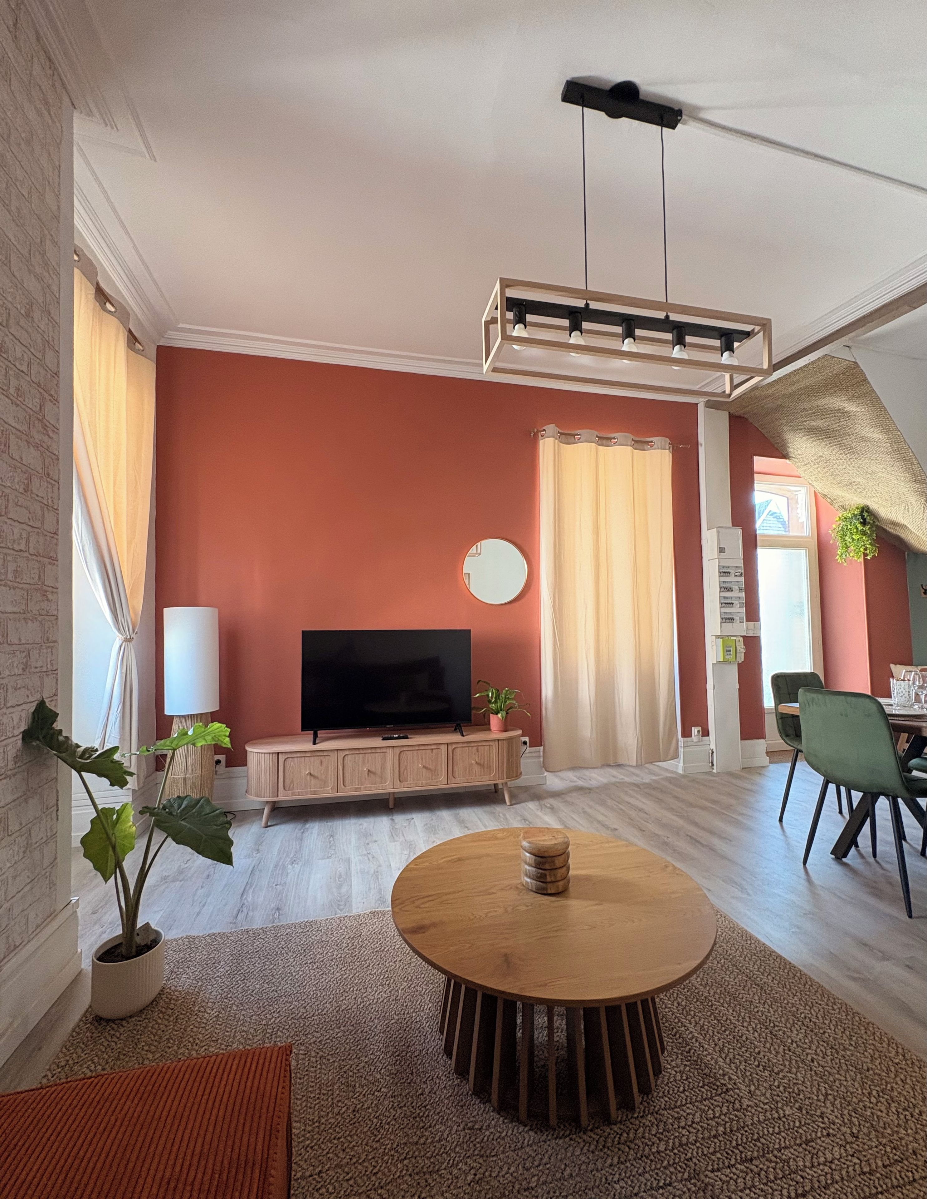 Una sala de estar con televisor de pantalla plana, muebles de madera, una mesa de centro redonda y una planta en maceta.