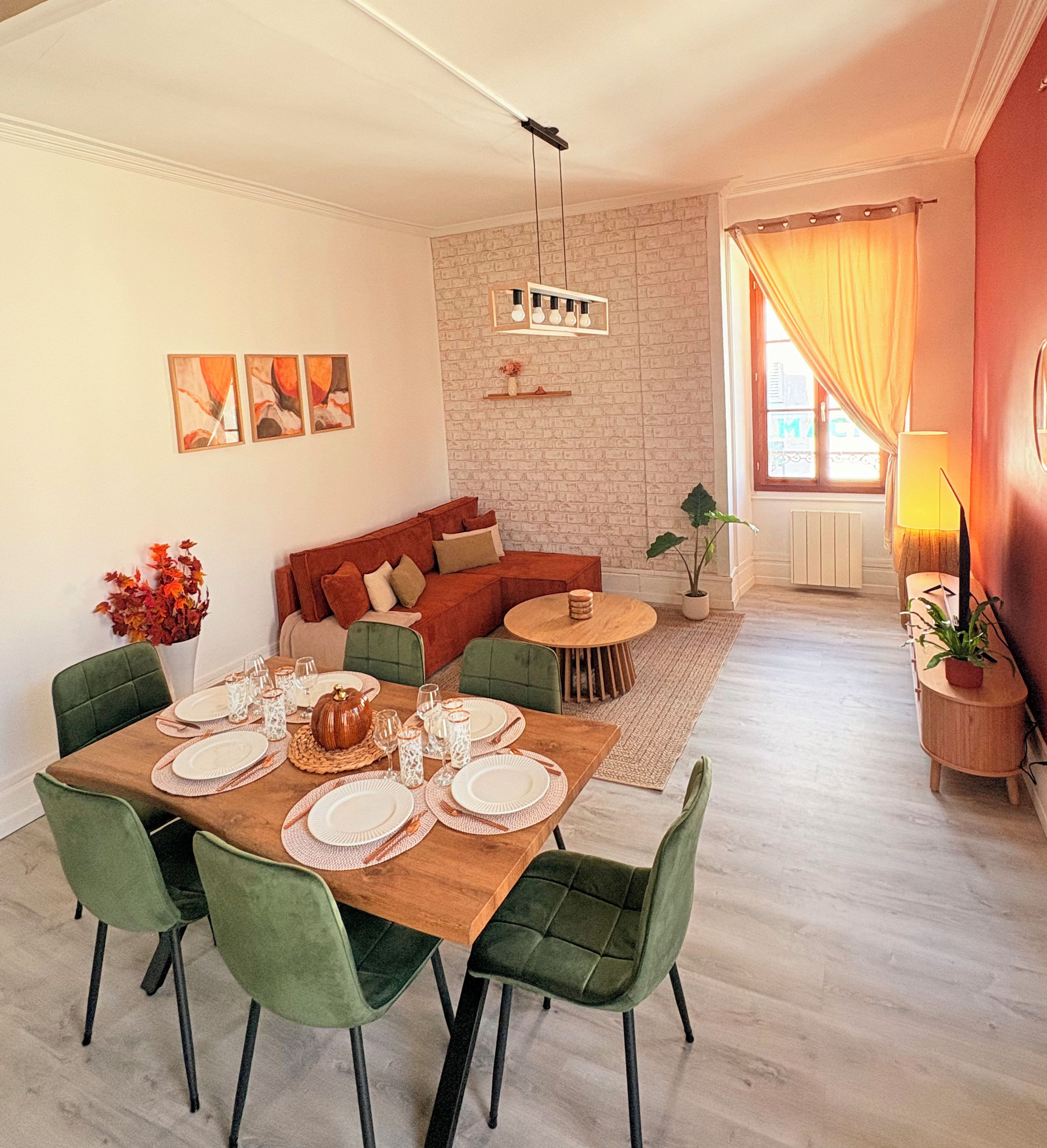 Comedor con mesa de madera dispuesta para cuatro personas, rodeada de sillas tapizadas en tonos verdes.