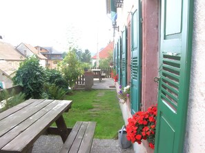 A courtyard with a wooden bench, a metal bucket, and a wall with green shutters. - Bed and Breakfast 'Chambre Double' with Mountain View, Shared Terrace and Wi-Fi (Thannenkirch)