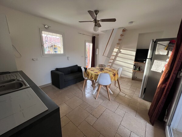 Ein kompakter Wohnbereich mit Küchenzeile, einem Essbereich mit Tisch und Stühlen, einer Couch und einem Deckenventilator.