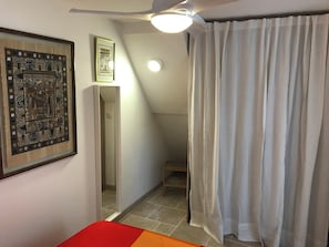 Ein Zimmer mit einem Bett, einem gerahmten Kunstwerk, einer Treppe und einem Vorhang.
