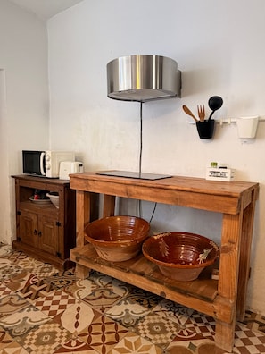 Una cocina con una mesa de madera, dos tazones de cerámica, un microondas y una lámpara fijada a la pared.