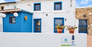 Un edificio blanco con puertas y ventanas azules, un letrero con el número 7 y plantas en macetas en el balcón.