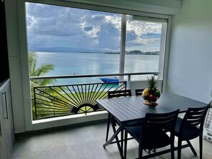 Ein Balkon mit Blick auf ein Gewässer, ein Esstisch mit Stühlen und eine Obstschale.