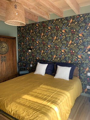 Quarto com cama, guarda-roupa de madeira, parede com padrão floral e luminária pendente.