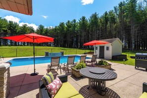 A backyard with a swimming pool, outdoor furniture, and a barbecue grill.