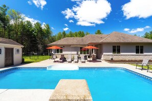 A swimming pool with a stone edge, surrounded by lounge chairs and umbrellas, with a house in the background.