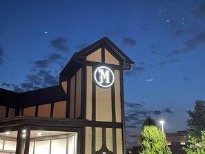 En byggnad med en tydlig logotyp i form av bokstaven ”M” på fasaden, en entré i hörnet och en gatlykta i närheten.
