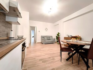 Een moderne keuken met een inbouwfornuis, een eethoek met een tafel en stoelen, en een woonkamer met een bank.