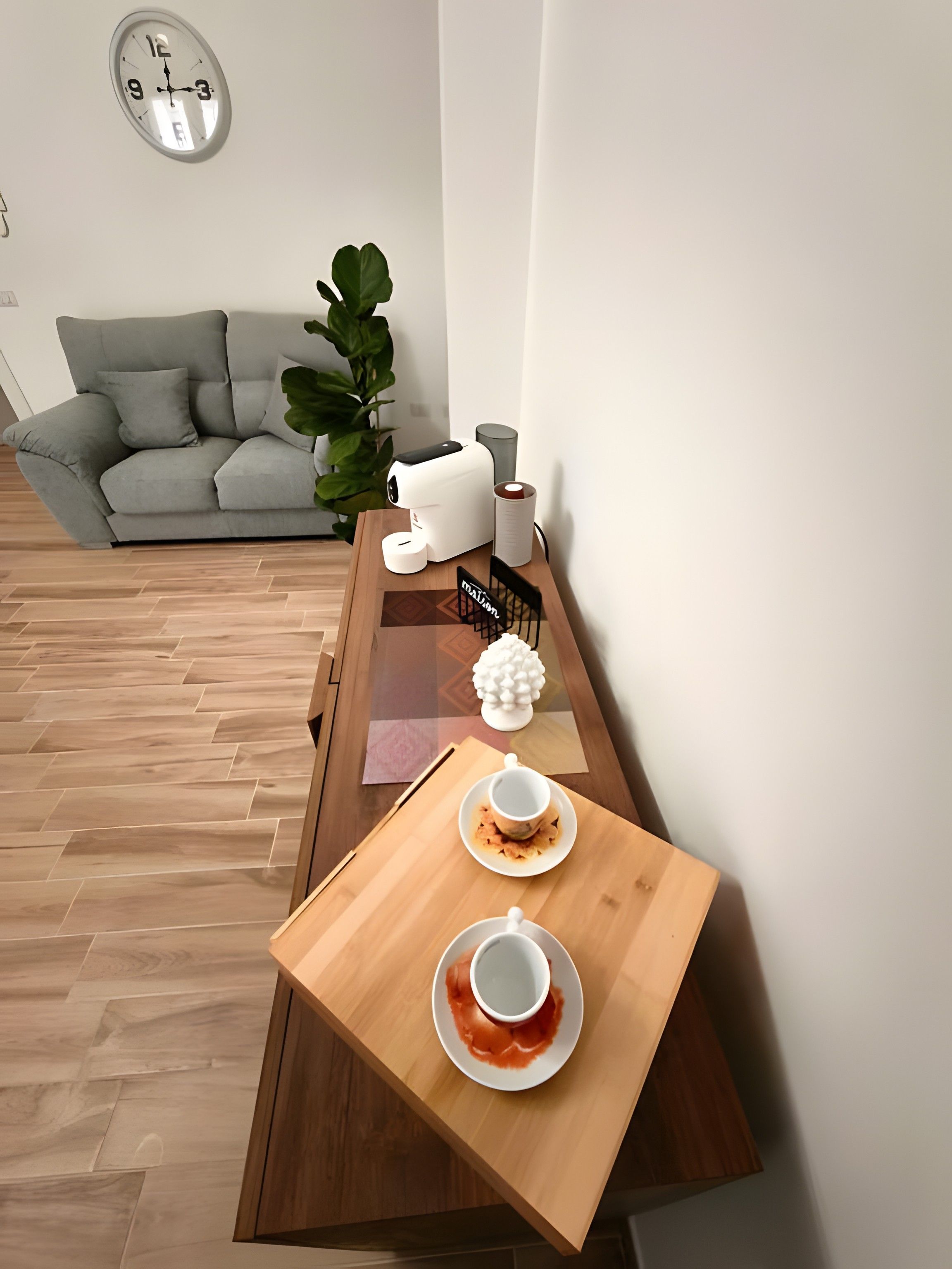 A modern living room with a sofa, a coffee table with a tea set, a plant, and a wall clock.