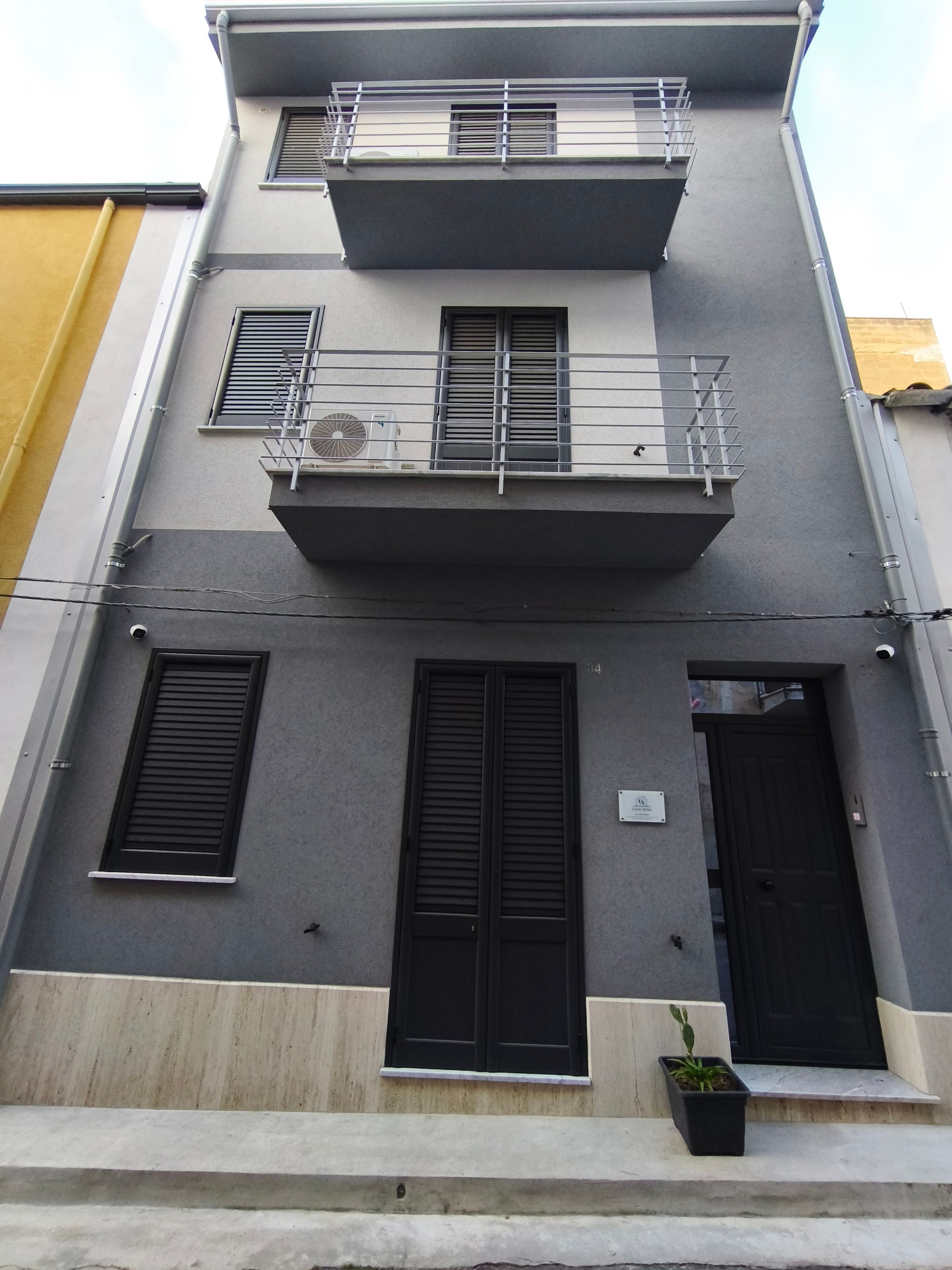 A multi-story building with a balcony, two windows with shutters, and a door.
