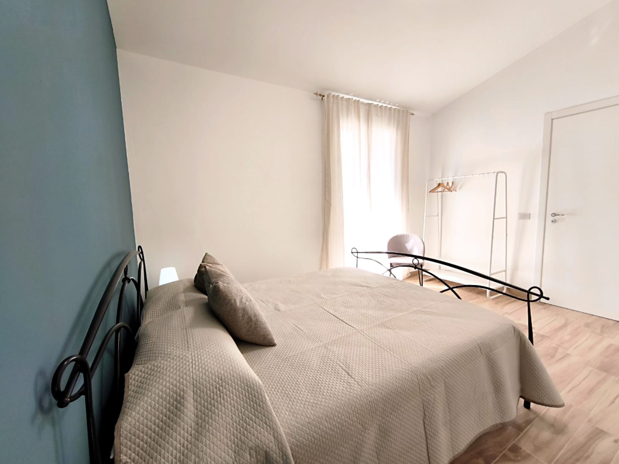 A bedroom with a bed, a chair, a wardrobe, and a window with curtains.