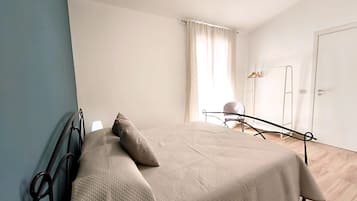 A bedroom with a bed, a chair, a wardrobe, and a window with curtains.
