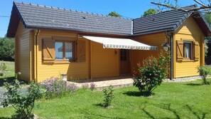 Uma casa de madeira com telhado inclinado, varanda coberta e um pequeno jardim com flores.