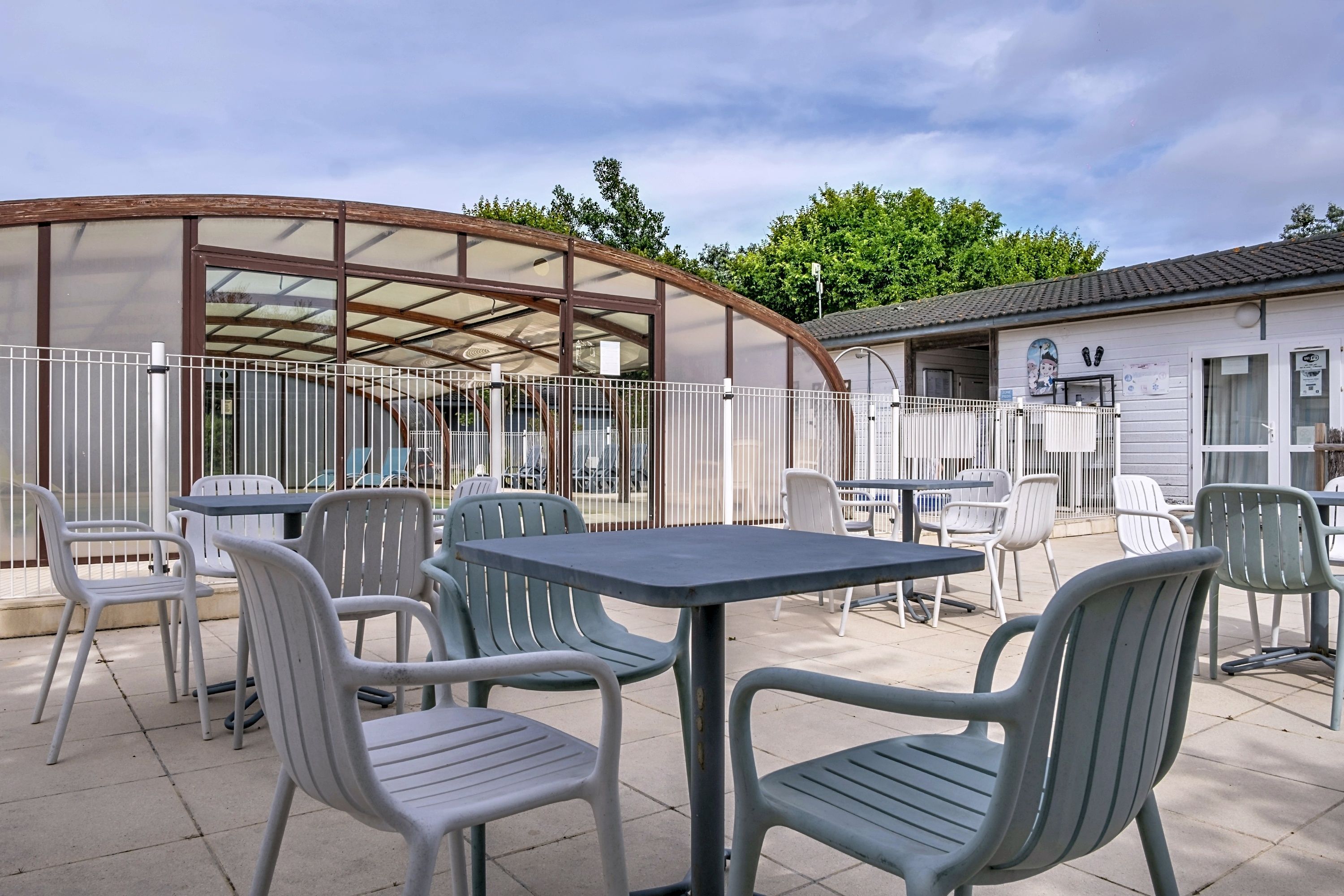 An outdoor patio area with tables and chairs, a covered seating area, and a building with a tiled roof.