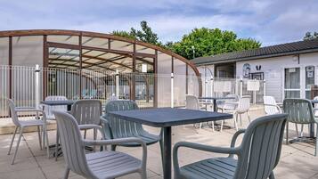 An outdoor patio area with tables and chairs, a covered seating area, and a building with a tiled roof.