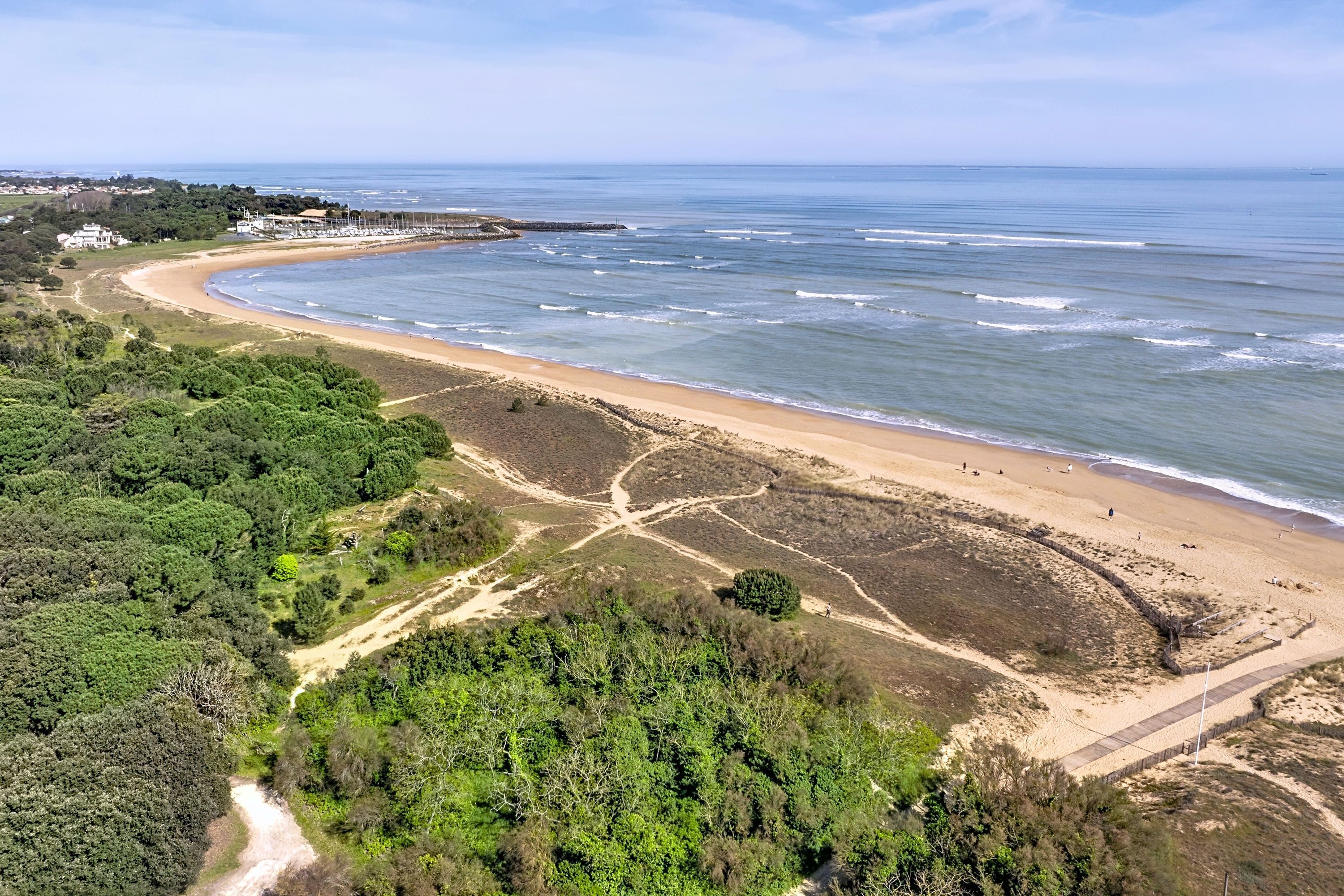 An aerial view of a coastal area with a sandy beach, a rocky shoreline, and dense greenery.