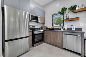Une cuisine moderne dotée d’appareils électroménagers en acier inoxydable, de meubles en bois et d’une fenêtre avec des stores.