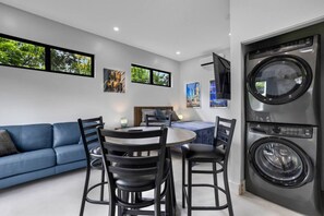 Un salon moderne avec un canapé bleu, une table de salle à manger ronde entourée de chaises, et un grand lave-linge et un sèche-linge fixés au mur.