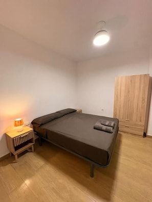 A single bed with a headboard, a bedside table with a lamp, and a wooden wardrobe in a room with wooden flooring and white walls. - Cami Real Hostel (Port de Sagunt)