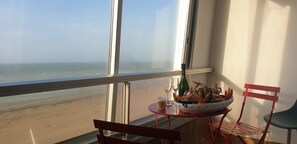 Ein Balkon mit Blick auf den Strand, ein Tisch mit einer Schüssel Meeresfrüchte, eine Flasche und zwei Gläser.