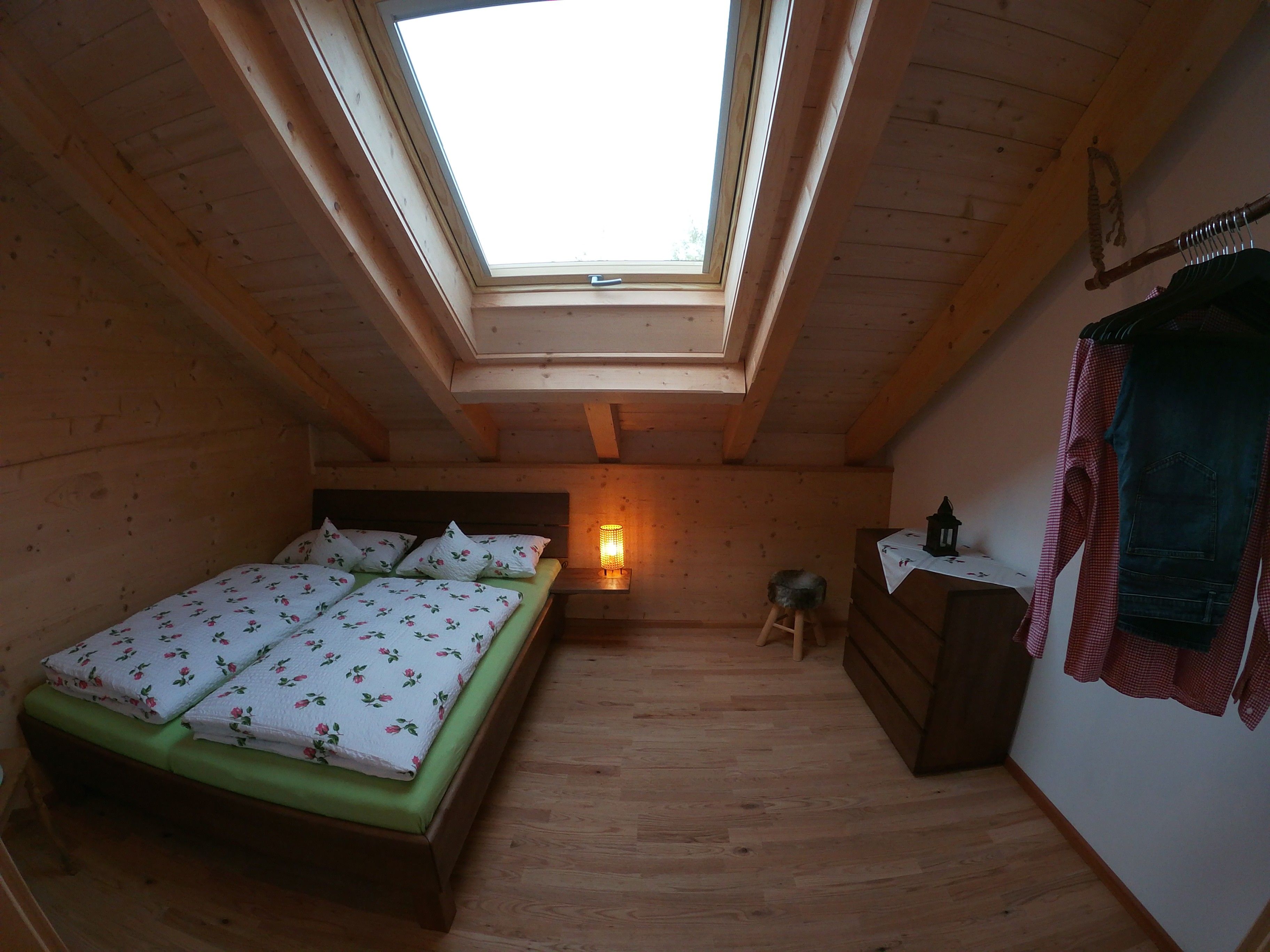 Ein kleiner, gemütlicher Raum mit Oberlichter, einem Bett mit floralem Bettzeug, einem Nachttisch mit Lampe und einer Holzkommode.