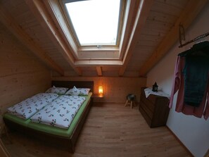 Ein kleiner, gemütlicher Raum mit Oberlichter, einem Bett mit floralem Bettzeug, einem Nachttisch mit Lampe und einer Holzkommode.