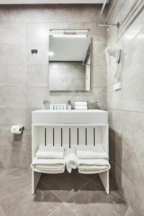 Un baño moderno con lavamanos blanco, espejo, toallero y secamanos.