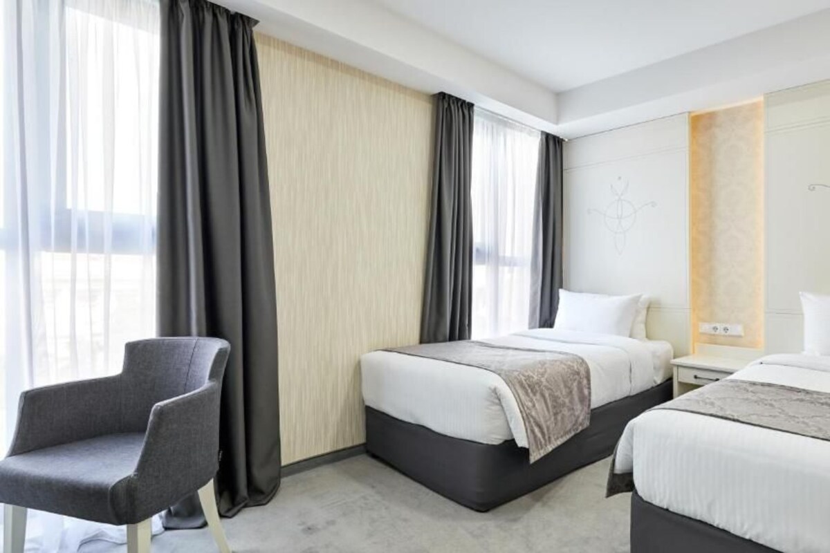 Habitación de hotel con dos camas, una silla y una mesita de noche.