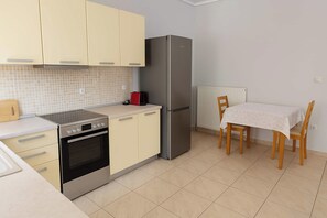 Eine kompakte Küche mit Herd, Backofen, Kühlschrank und einem Esstisch mit Stühlen.