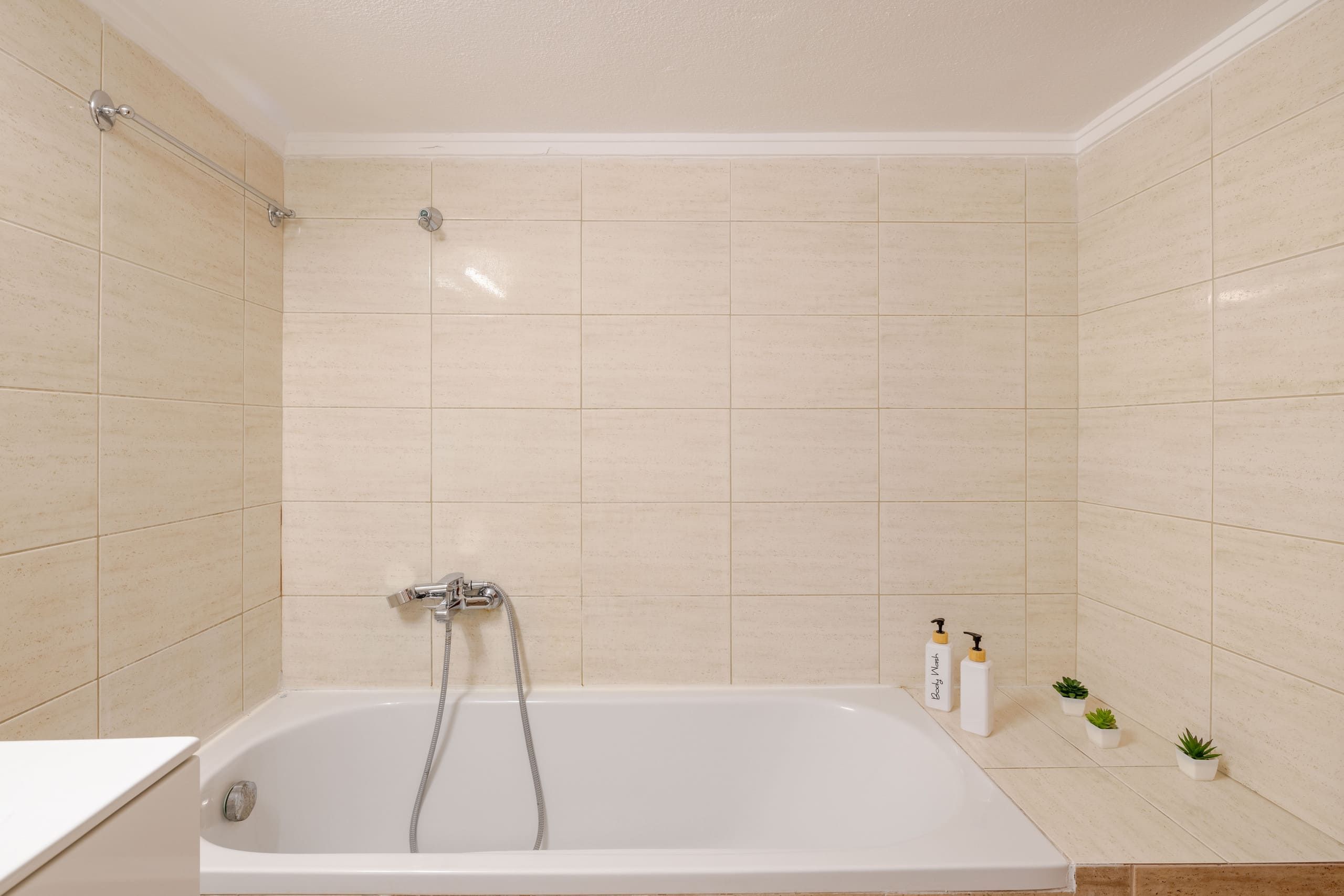 Une salle de bain avec une baignoire, une douche et deux bouteilles de gel douche posées sur le sol.