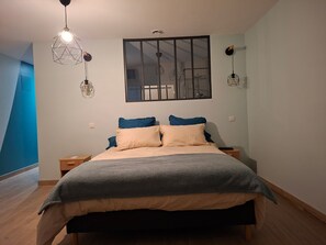 Une chambre à coucher comprenant un lit, deux tables de chevet, un luminaire suspendu et une fenêtre avec des stores.
