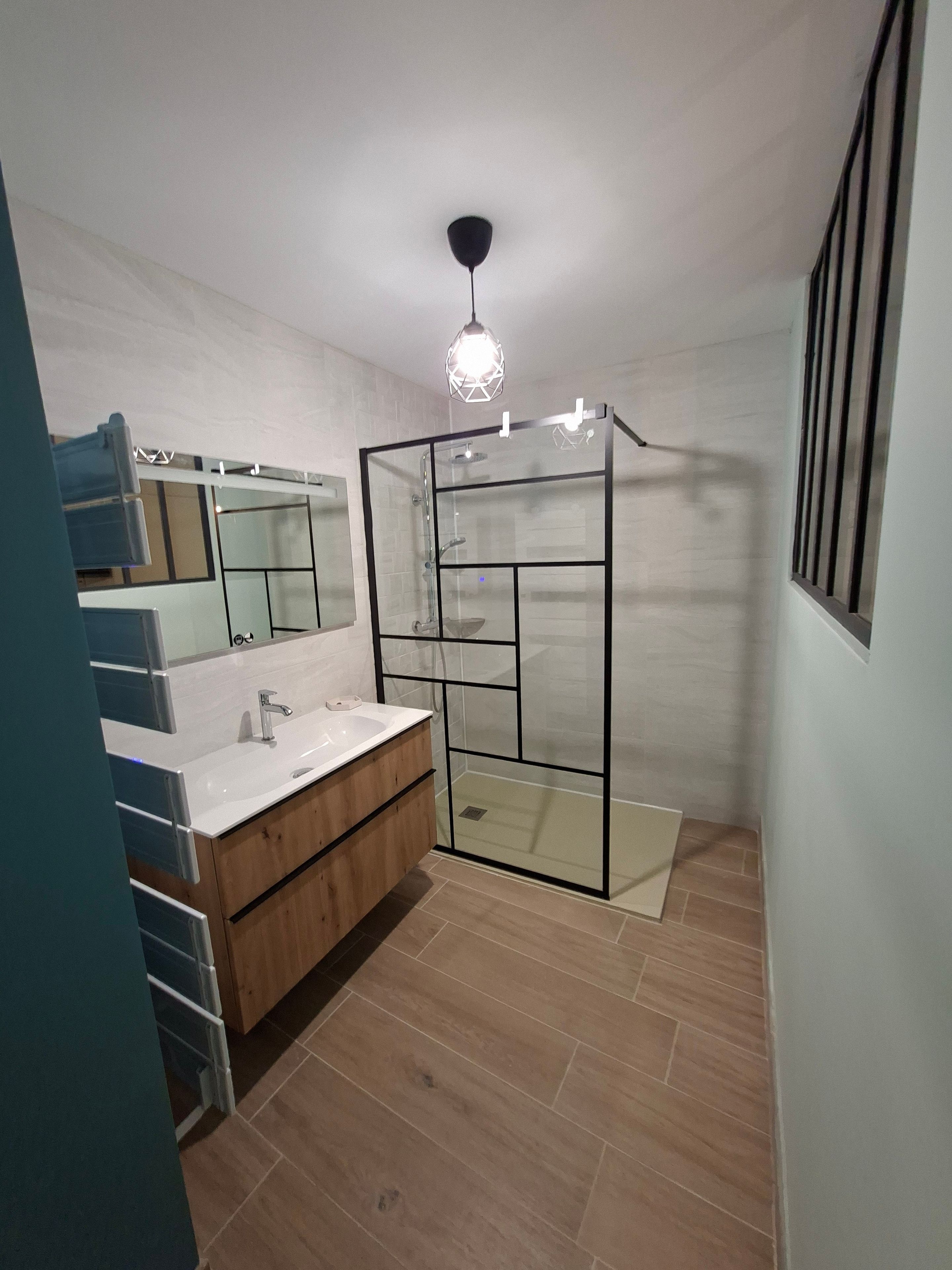 A modern bathroom with a glass shower enclosure, a white sink with a wooden vanity, and a mirror above the sink.
