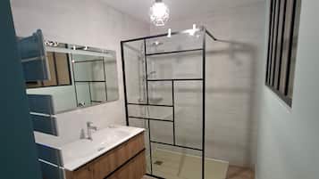 A modern bathroom with a glass shower enclosure, a white sink with a wooden vanity, and a mirror above the sink.