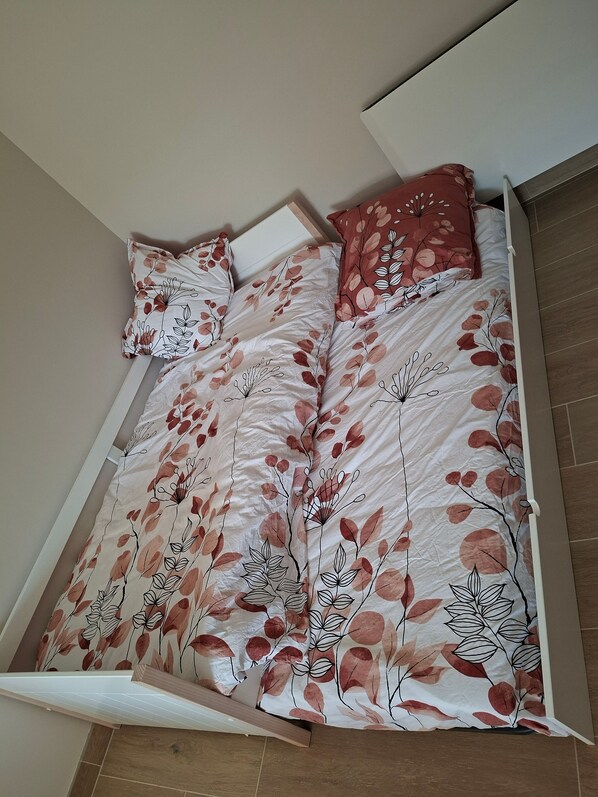 Ein Bett mit einem Blumenmuster, einem Holzkopfstück und einem roten Kissen.