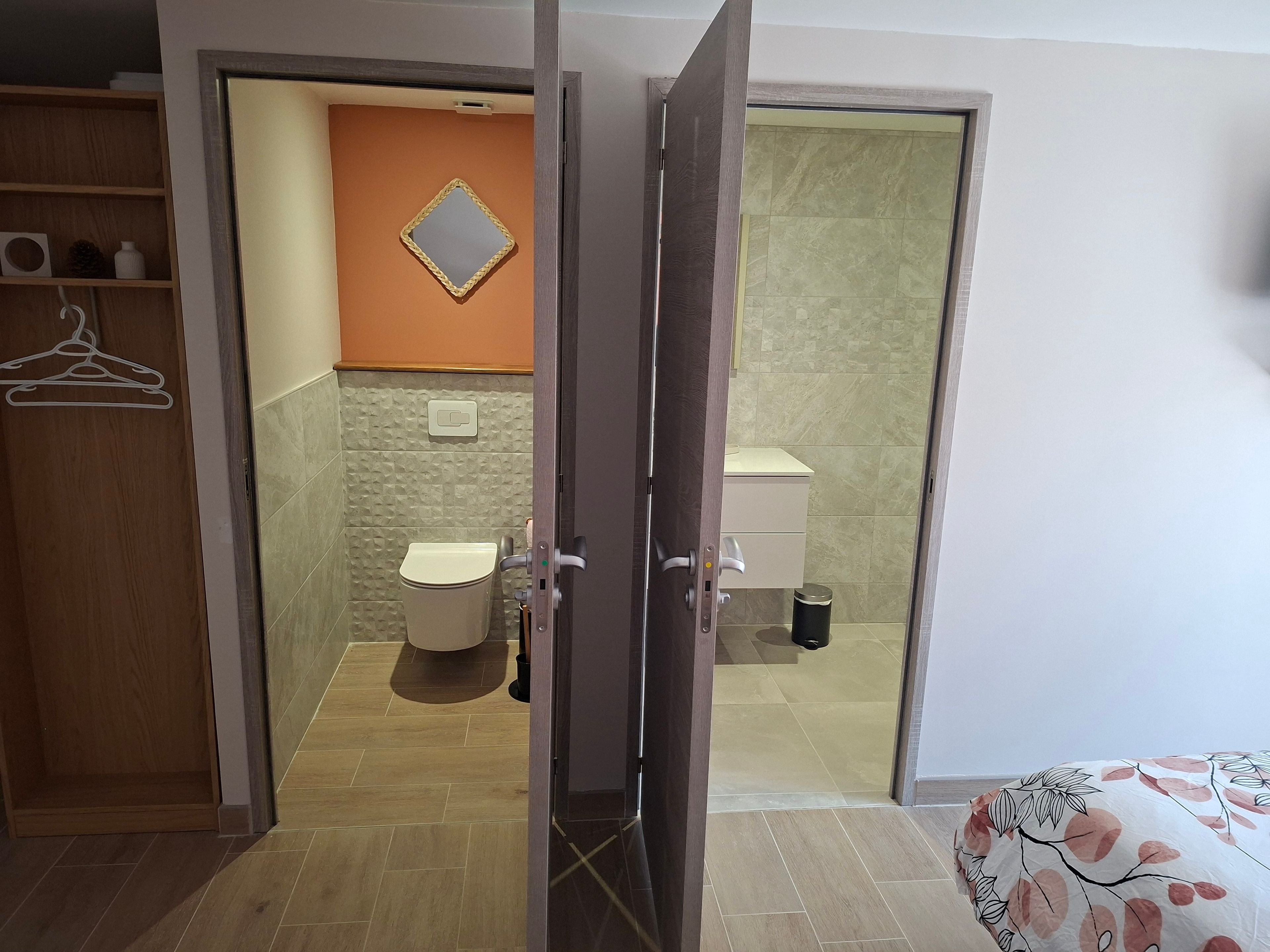 Une chambre avec une armoire en bois, des toilettes et un lit recouvert d’une couvre-lit à motifs floraux.