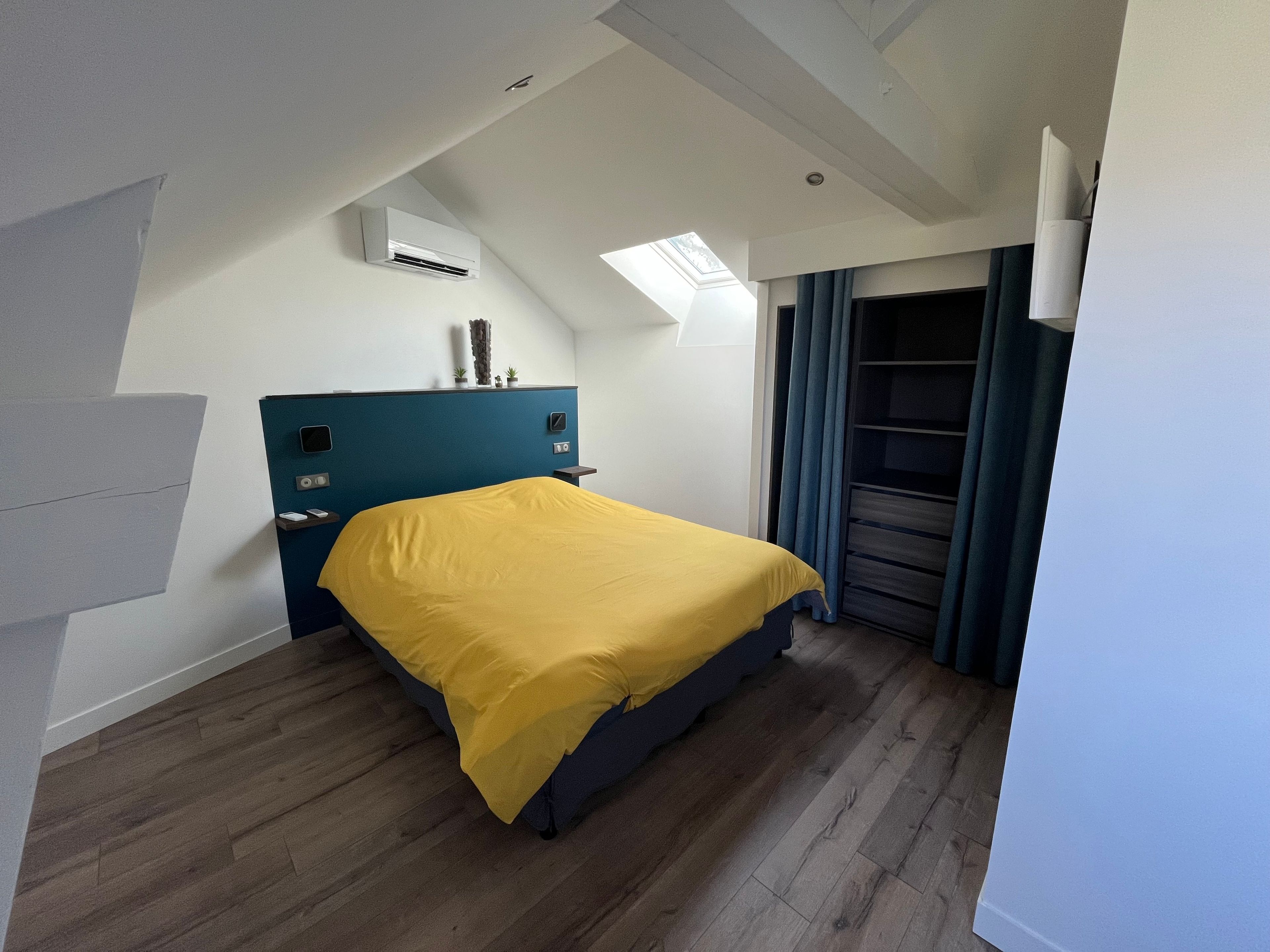 Et hotelværelse med seng, indbygget aircondition, ovenlys, garderobeskab og et vindue med gardiner.