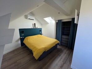 Habitación de hotel con cama, aire acondicionado integrado, tragaluz, armario y ventana con cortinas.