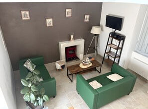 Una sala de estar con sofás verdes, una chimenea, un televisor y cuadros en la pared.