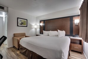 A hotel room with a large bed, a desk, a chair, a bedside table, a lamp, a picture on the wall, and a window with curtains. - 1625 French Camp Turnpike (Stockton)