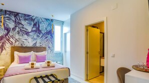 Une chambre d’hôtel avec un lit, une tête de lit, un mur orné d’une fresque représentant des feuilles tropicales, une porte donnant sur une autre pièce et une petite table avec un plateau.