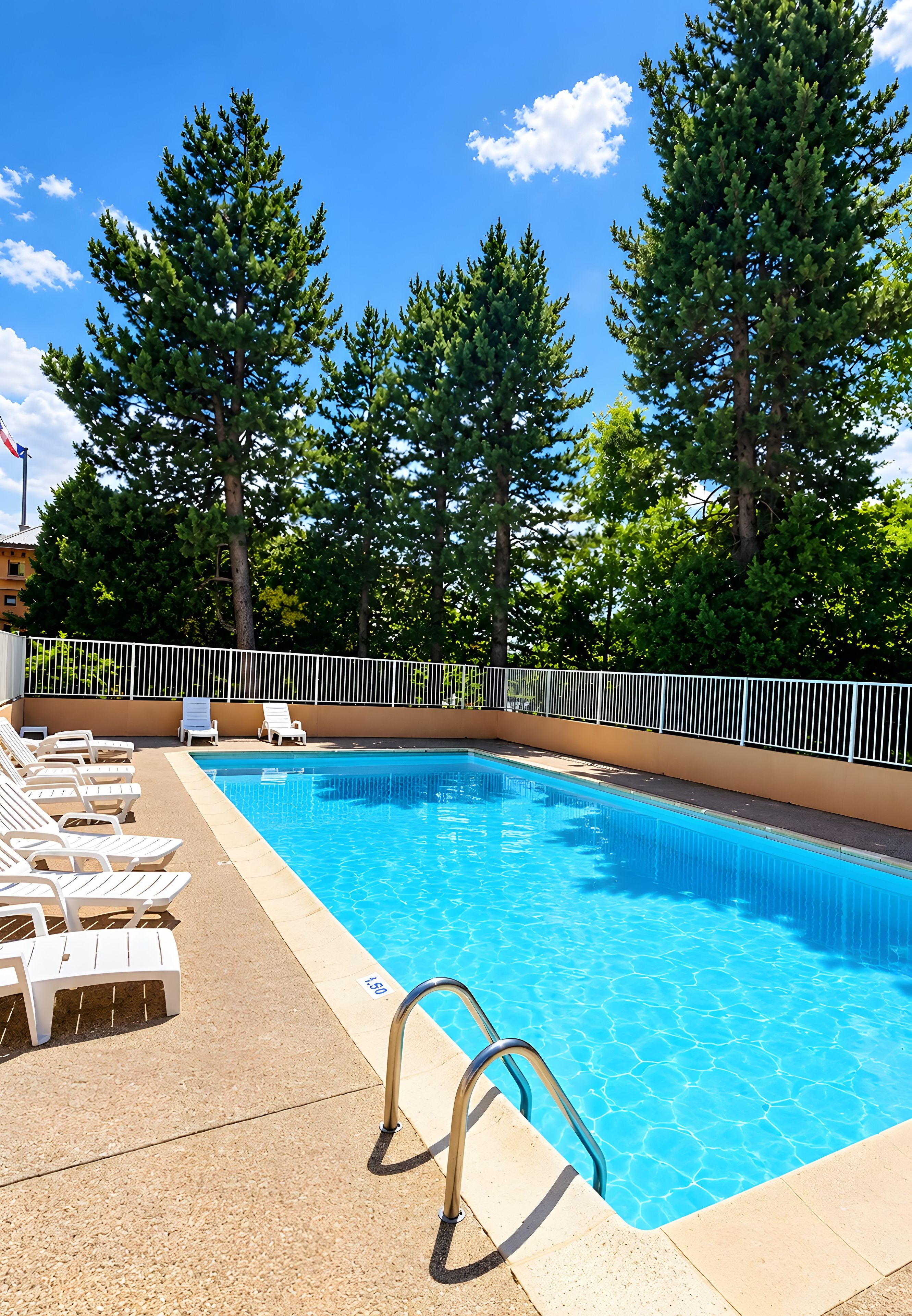 A swimming pool with clear blue water, surrounded by white lounge chairs and a metal fence.
