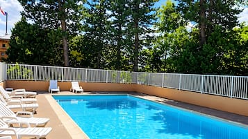 A swimming pool with clear blue water, surrounded by white lounge chairs and a metal fence.